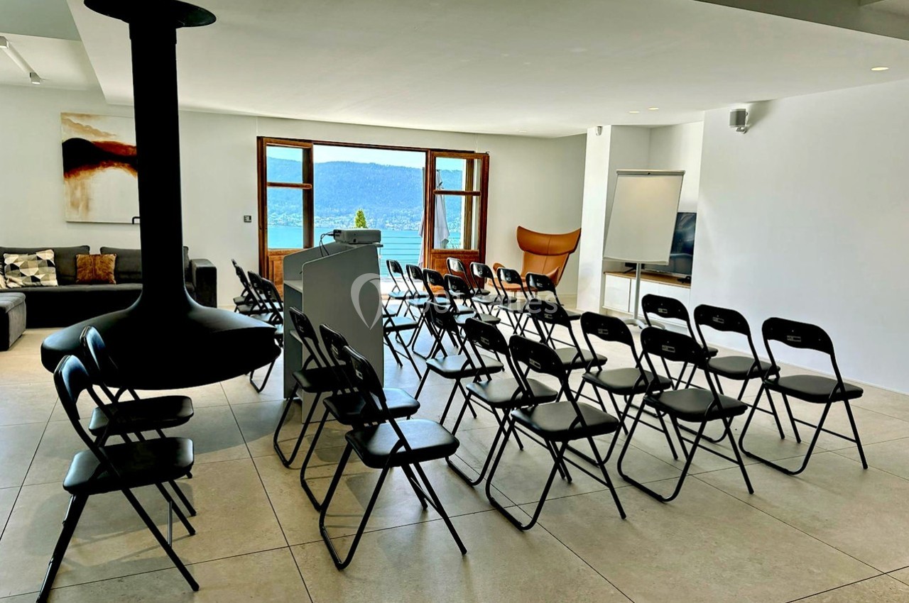 Salle lumineuse aménagée pour une présentation, avec des chaises pliantes alignées face à un pupitre et un tableau blanc.