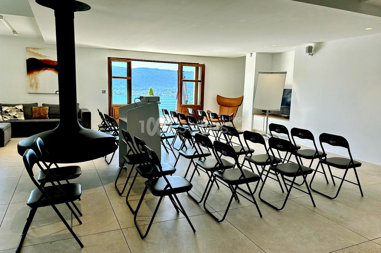 Salle lumineuse aménagée pour une présentation, avec des chaises pliantes alignées face à un pupitre et un tableau blanc.