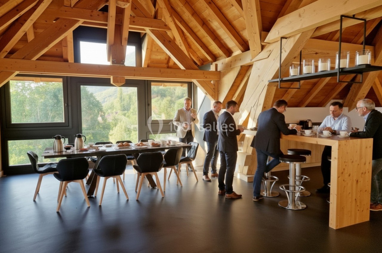 Des hommes en costume discutent autour d'un comptoir en bois dans une salle lumineuse avec une grande table et des fenêtres…