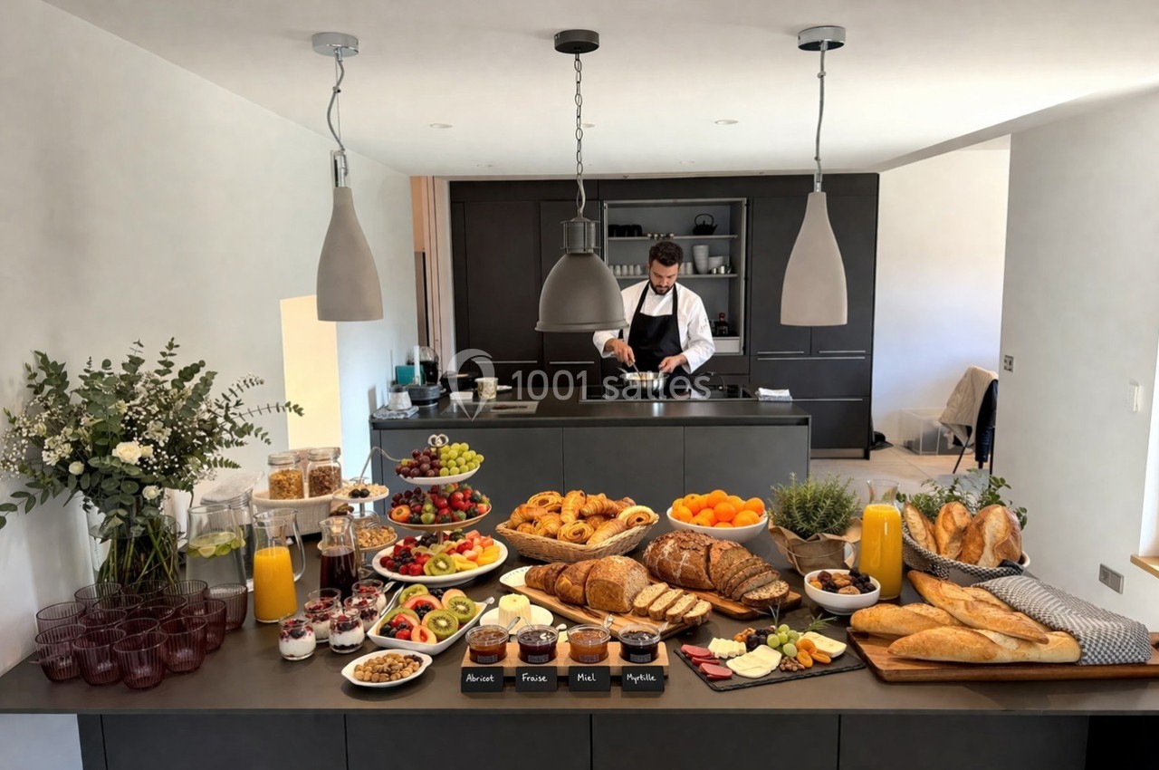Buffet de petit-déjeuner avec fruits, viennoiseries, pains, jus et yaourts, un chef cuisine en arrière-plan.