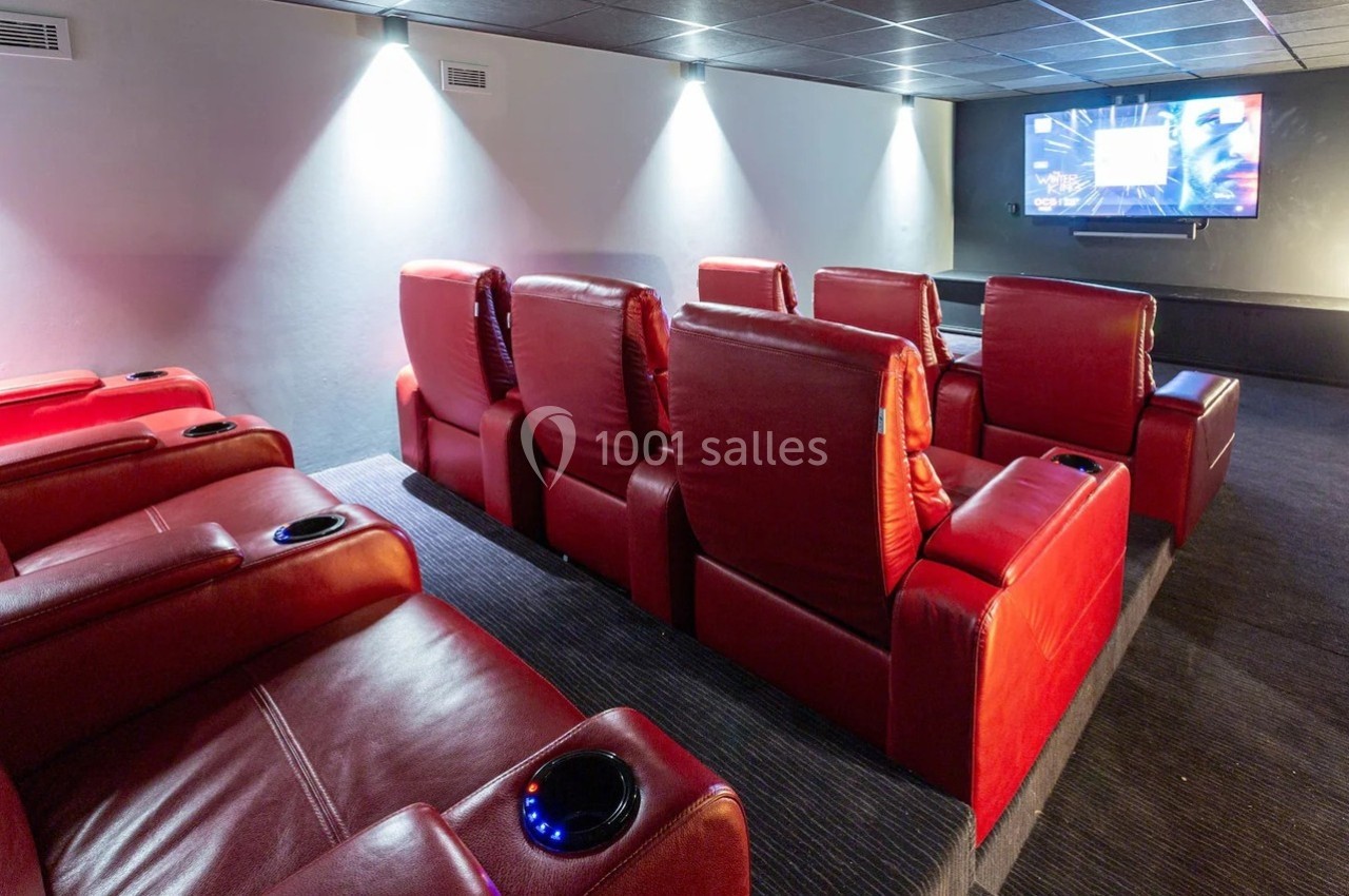 Salle de cinéma privée avec fauteuils rouges inclinables et écran de projection allumé sur un mur blanc.
