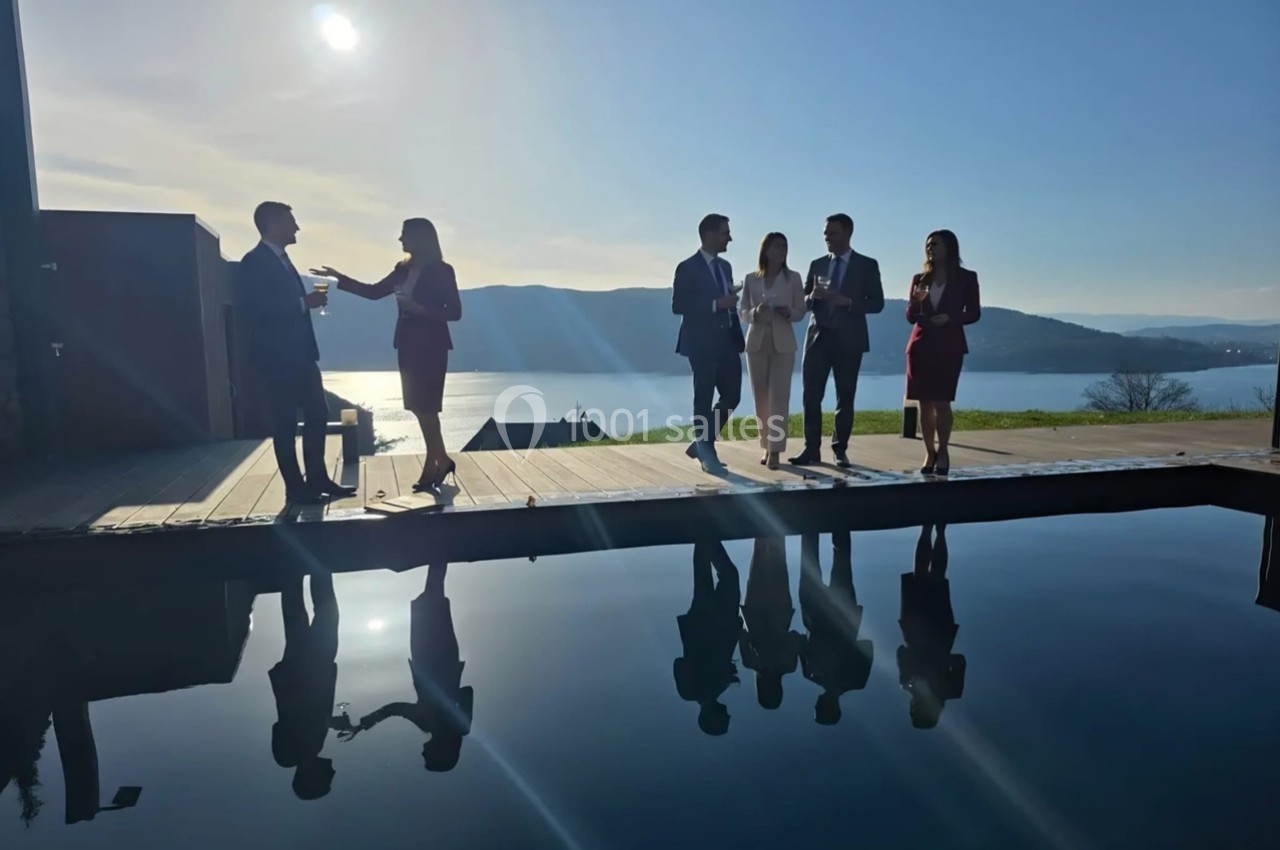 Un groupe de personnes en tenue professionnelle discute près d'une piscine avec vue sur un lac au coucher du soleil.