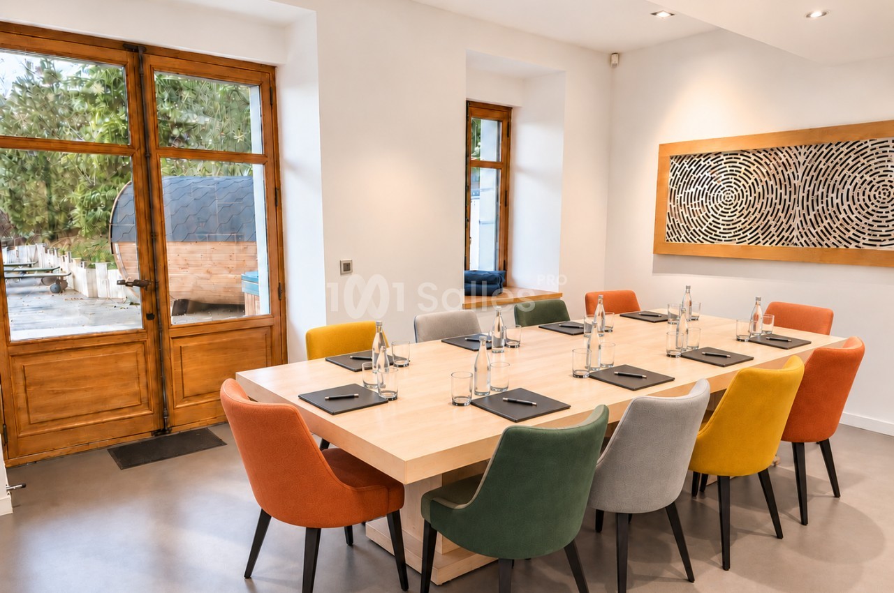 Salle de réunion dressée avec table en bois et chaises colorées - accès terrasse vitré.