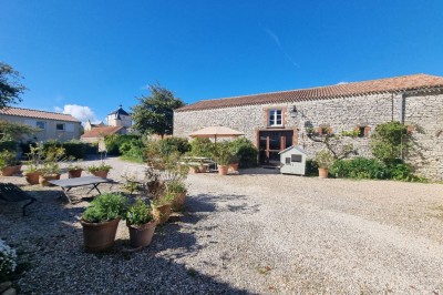Salle lumineuse avec murs en pierre, grande table en bois, chaises noires et décorations murales, éclairée par des fenêtres.