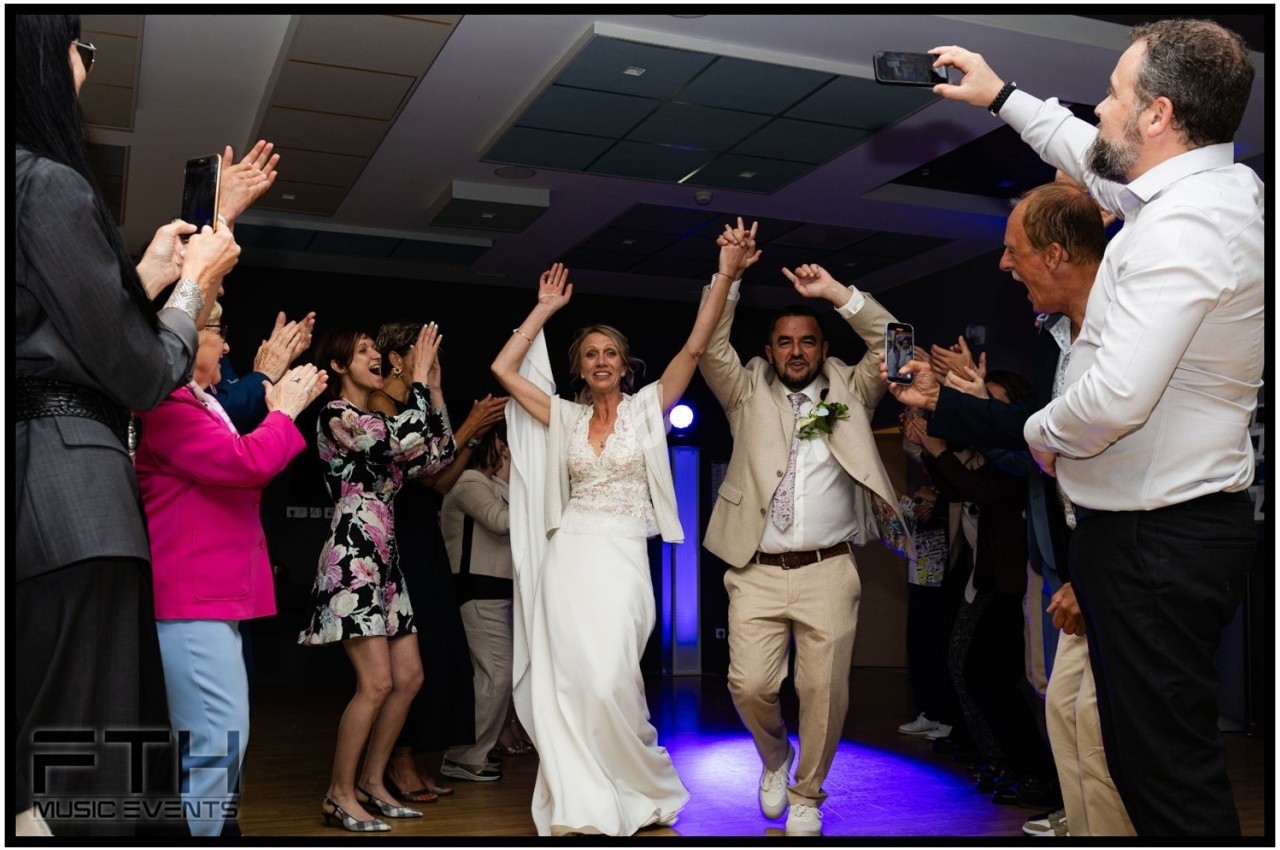 Un couple de mariés danse joyeusement entouré d'invités applaudissant dans une salle de réception.