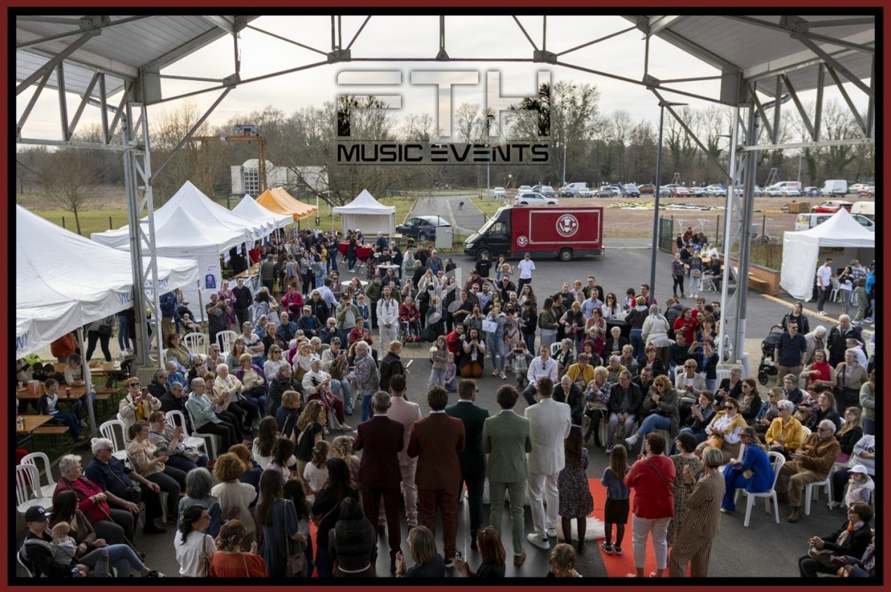 Un groupe de musiciens joue devant un public assis et debout sous une structure couverte en plein air.