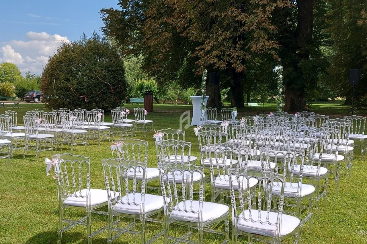 Chaises transparentes alignées en extérieur sur une pelouse, disposées pour une cérémonie sous un ciel dégagé.