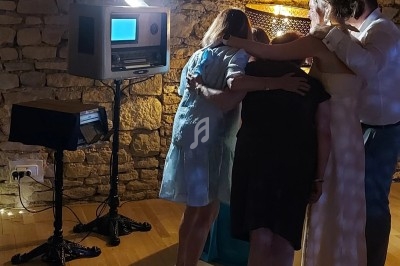 Quatre personnes regardent un écran lumineux dans un photomaton rétro, dans une pièce aux murs en pierre.