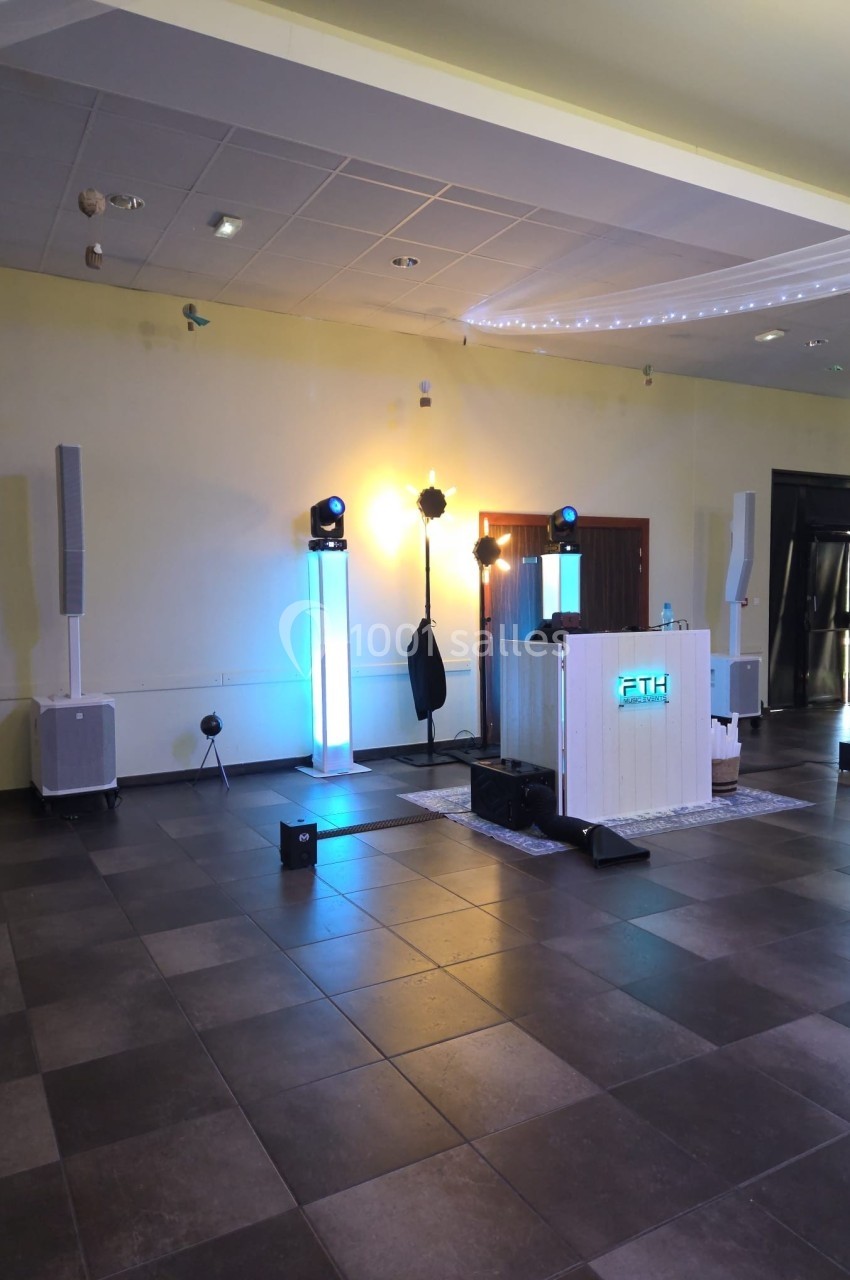 Installation de matériel de sonorisation et éclairage dans une salle vide avec sol carrelé et plafond suspendu.
