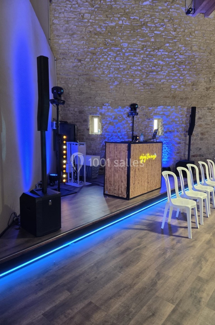 Scène avec équipement de DJ, éclairage bleu et chaises blanches alignées dans une salle aux murs en pierre.