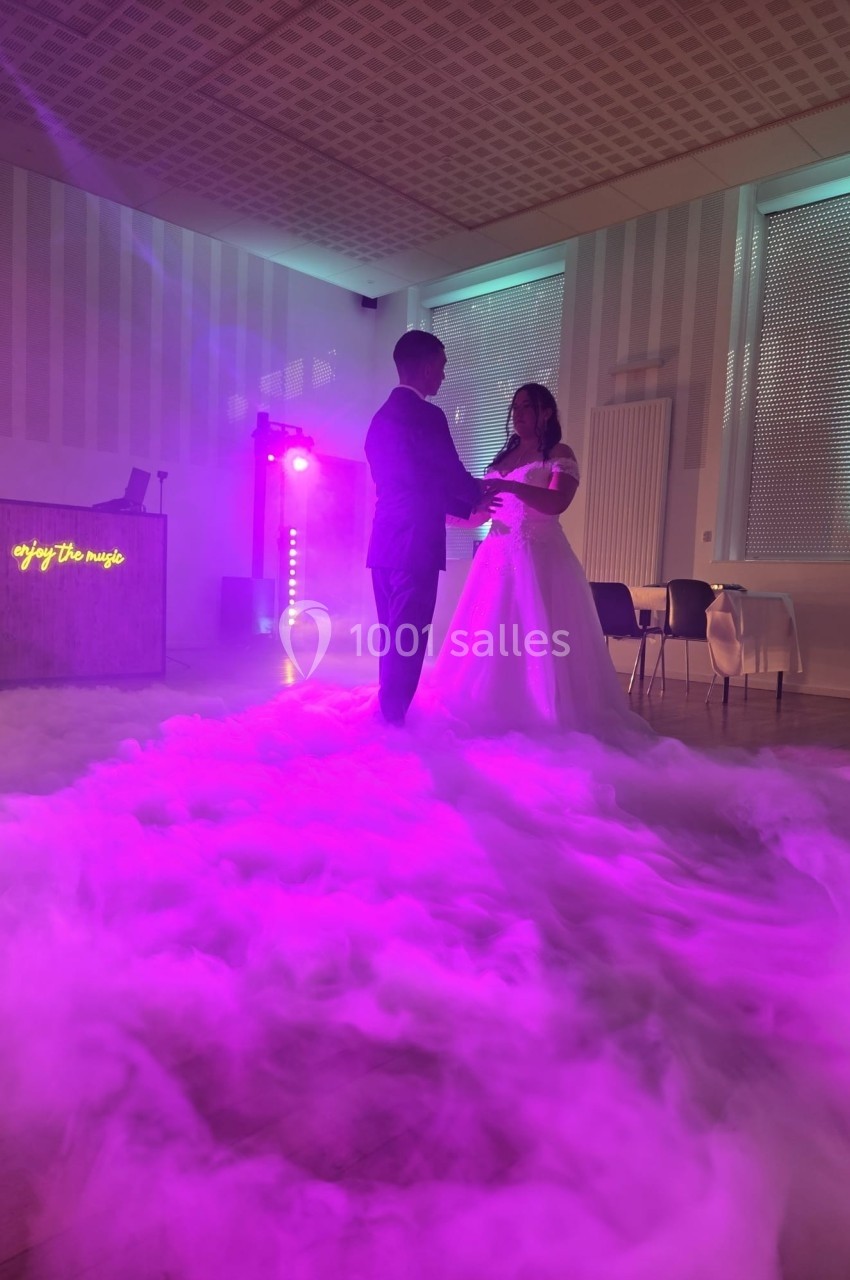 Un couple danse sur une piste enveloppée de fumée et éclairée par des lumières violettes dans une salle.