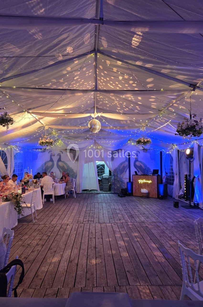 Intérieur d'une tente éclairée avec des guirlandes lumineuses, tables dressées et décorations suspendues pour un événement.
