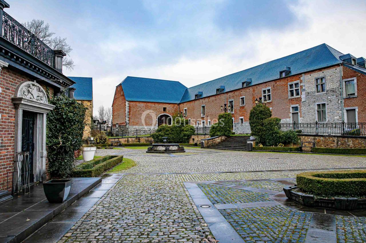 Cour pavée avec fontaines, entourée de bâtiments en briques et pierres, sous un ciel nuageux.