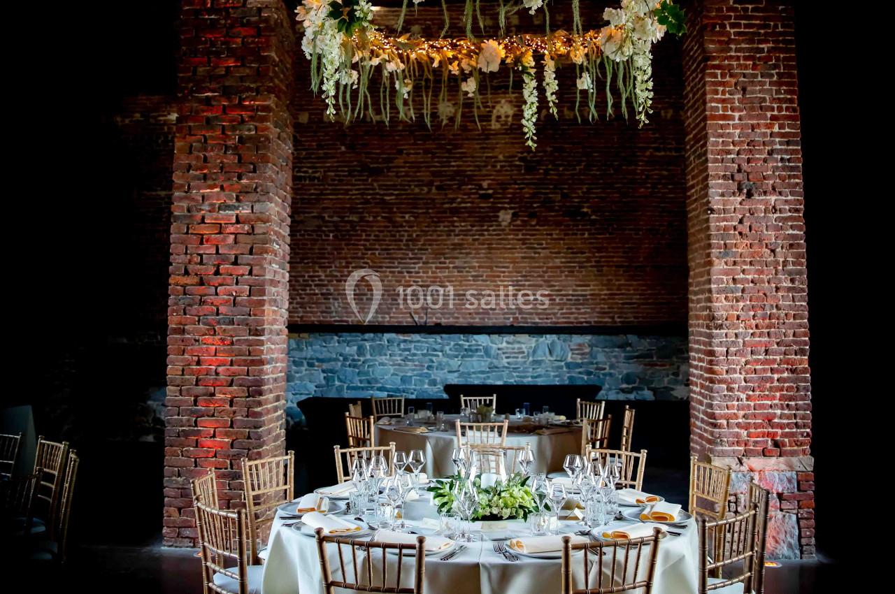 Table ronde élégamment dressée avec des chaises en bois, sous un lustre floral suspendu dans une salle en briques.