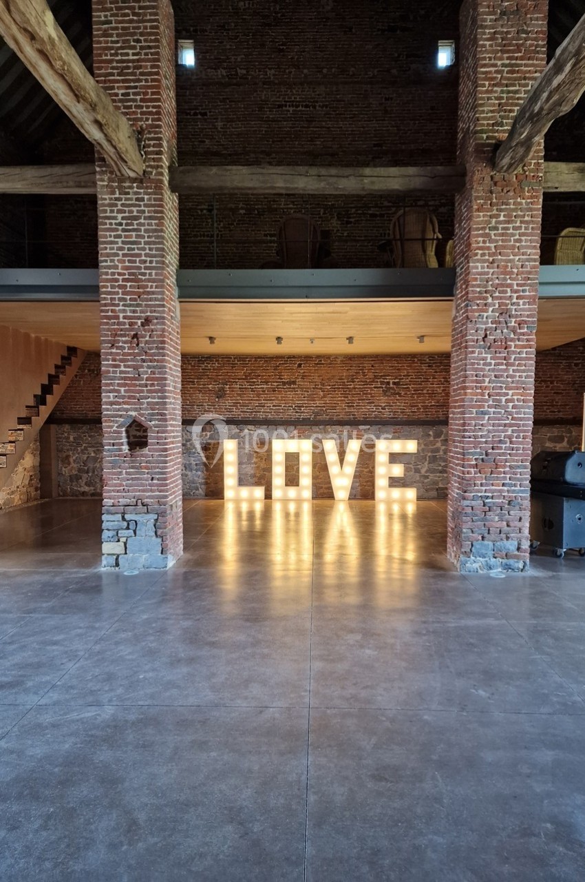 Grange en briques avec des lettres lumineuses formant le mot ’LOVE’ au centre de l'espace.