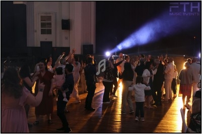 Des personnes dansent et socialisent dans une salle éclairée par des projecteurs, créant une ambiance festive.