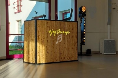 Console DJ en bois avec l'inscription lumineuse ’enjoy the music’, éclairée par la lumière naturelle dans une salle.
