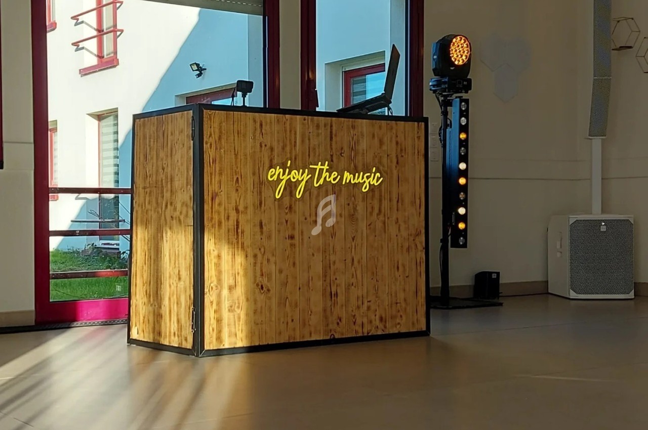 Console DJ en bois avec l'inscription lumineuse ’enjoy the music’, éclairée par la lumière naturelle dans une salle.