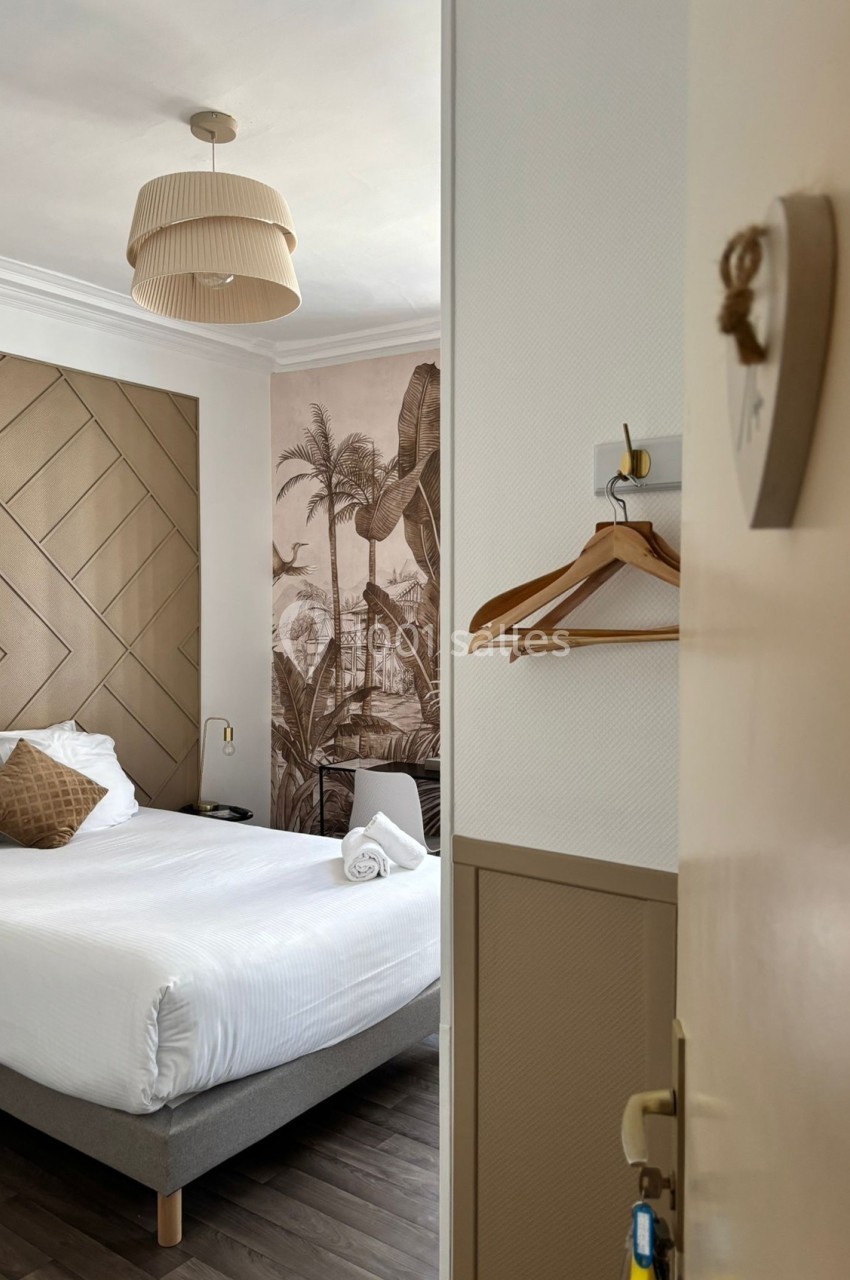 Chambre lumineuse avec lit double, décoration murale tropicale, cintres suspendus et éclairage moderne.