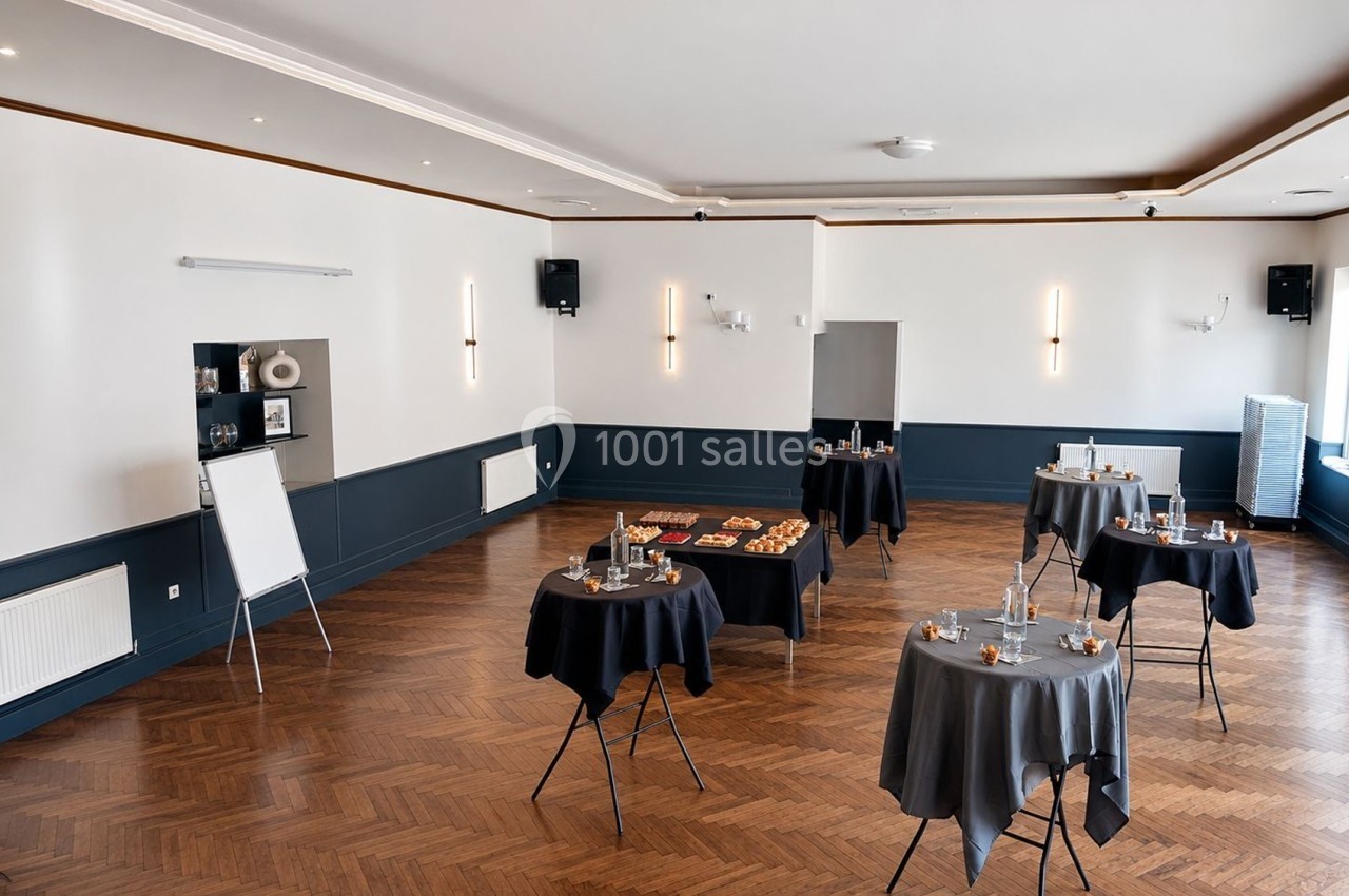 Salle lumineuse avec parquet en bois, tables hautes couvertes de nappes noires, disposées pour un événement.