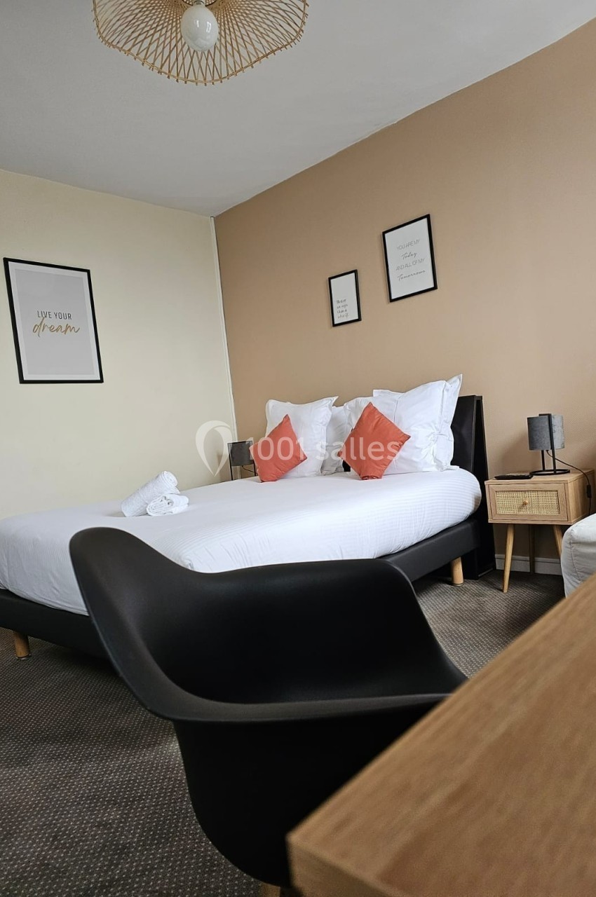 Chambre avec lit double, coussins orange, murs beige et blanc, décor minimaliste et mobilier moderne.