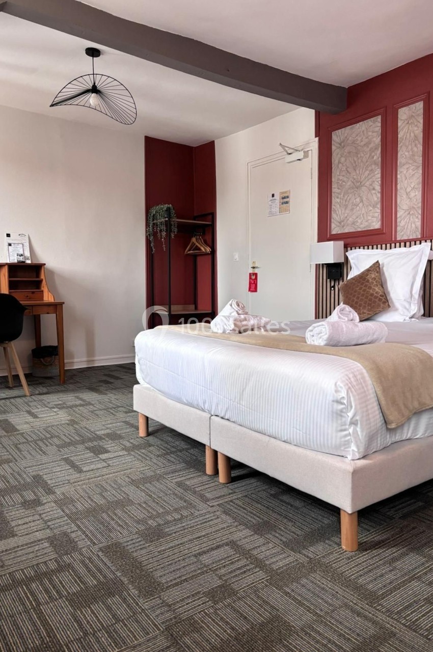 Chambre d'hôtel avec lit double, bureau en bois, chaise noire, et décoration murale rouge et beige.