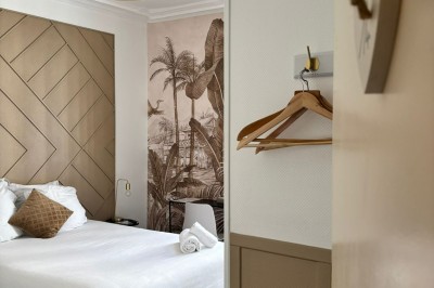 Miniature Location salle Bernay (Eure) - Hôtel du Lion d'Or #7 Chambre d'hôtel lumineuse avec lit double, linge blanc, décoration murale tropicale et cintres accrochés au mur.
