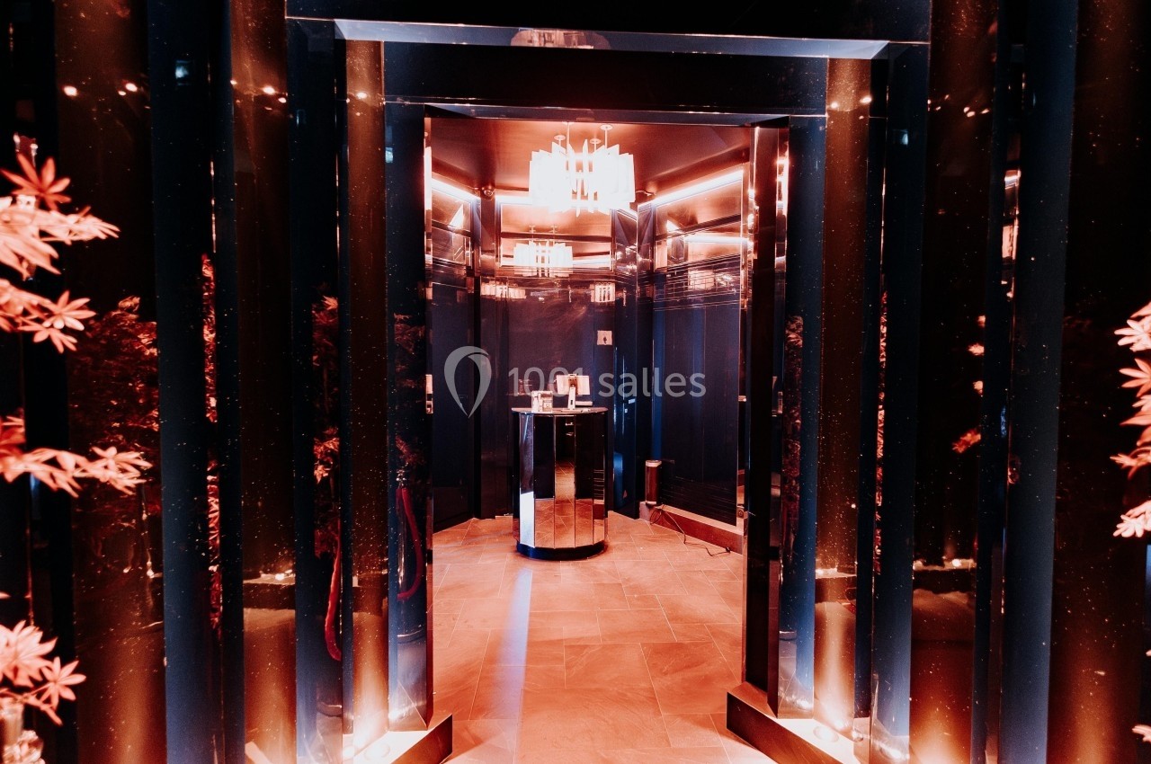 Couloir sombre avec murs brillants noirs, éclairage chaleureux et lustre moderne au plafond.