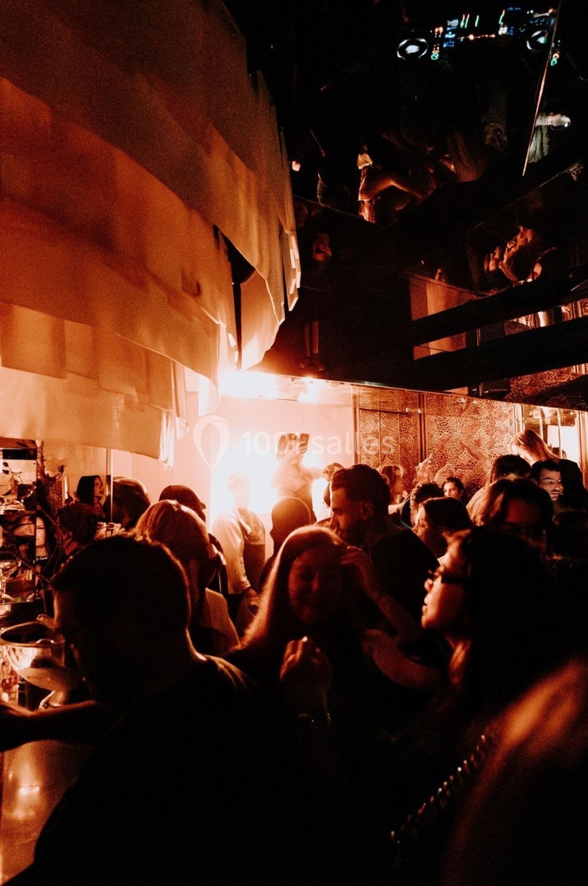 Foule rassemblée dans un bar ou club à l'éclairage tamisé et ambiance chaleureuse.