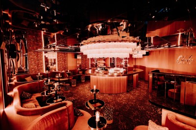 Bar illuminé avec un grand lustre suspendu, vu à travers une vitre floue dans une ambiance tamisée.