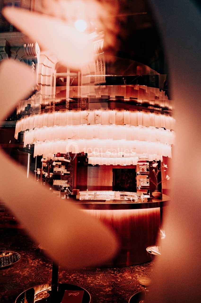 Bar illuminé avec un grand lustre suspendu, vu à travers une vitre floue dans une ambiance tamisée.