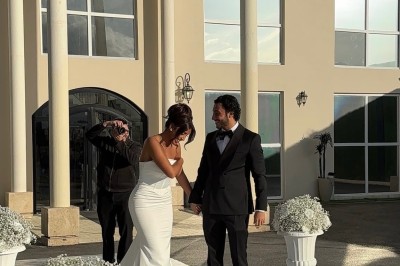 Un couple en tenue de mariage se tient devant un bâtiment élégant sous un ciel dégagé.