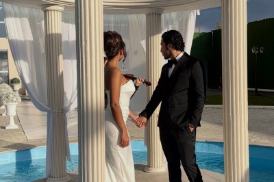 Un couple en tenue de mariage se tient devant un bâtiment élégant sous un ciel dégagé.