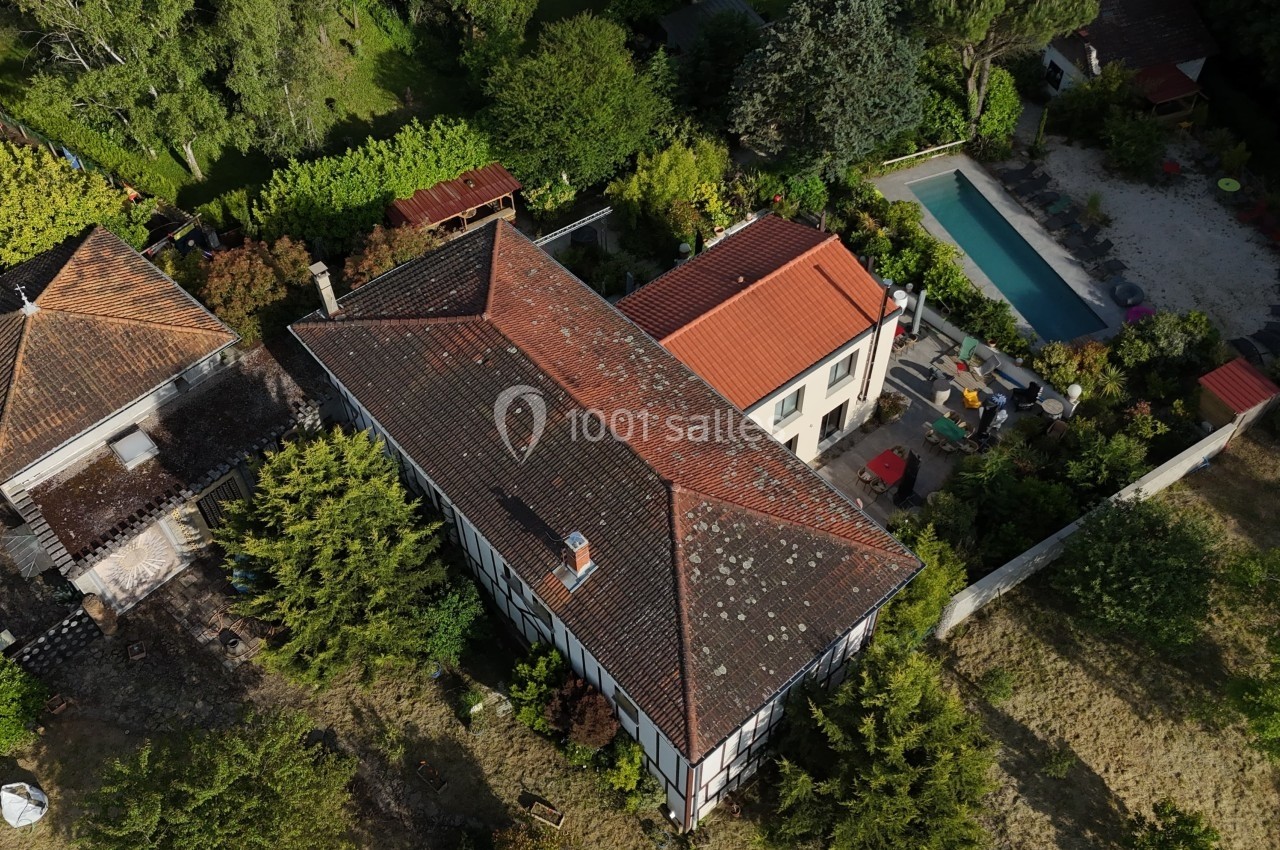 Vue aérienne d'une maison avec toit en tuiles, jardin arboré, piscine et dépendances dans un cadre résidentiel.