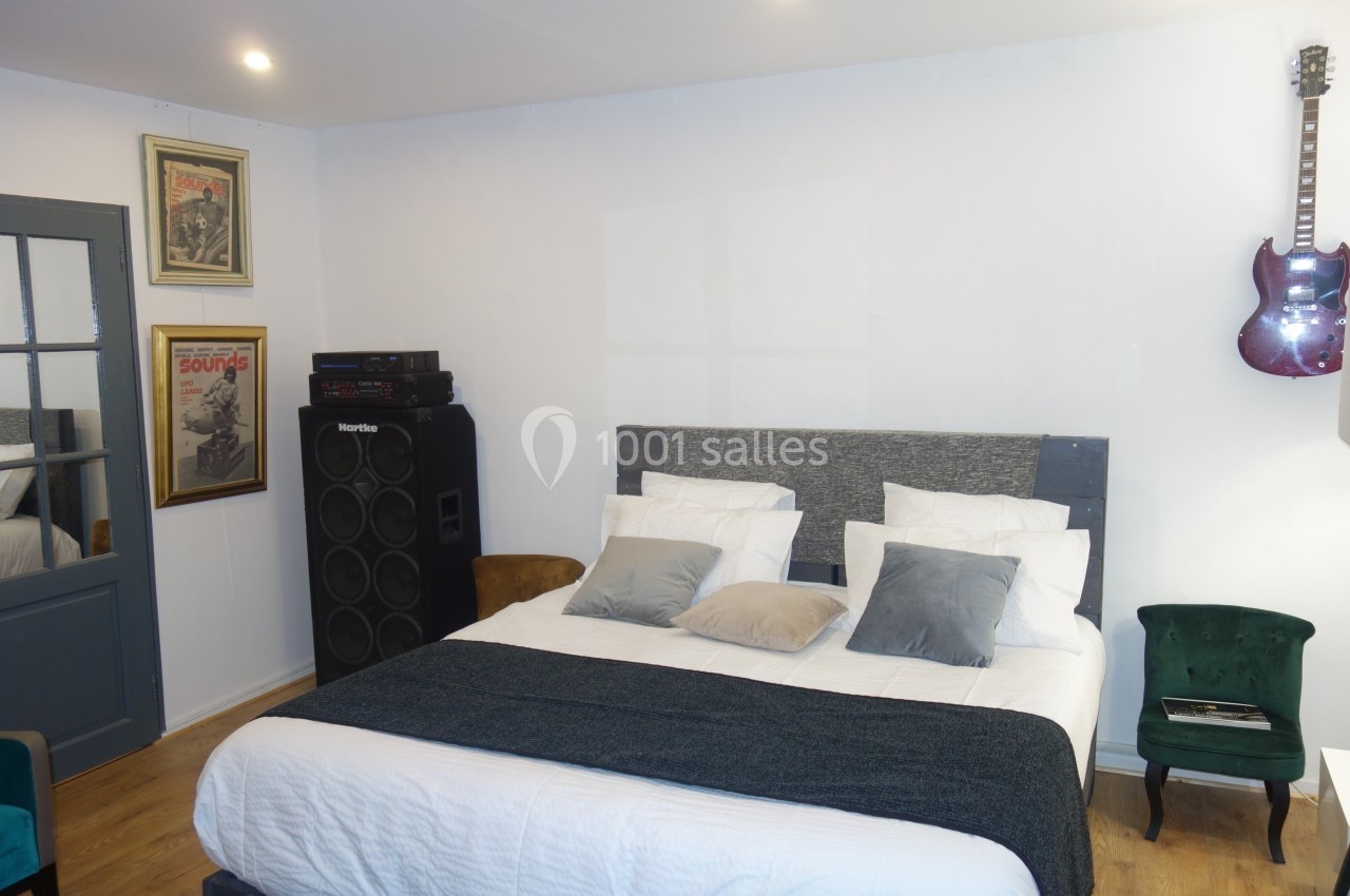 Chambre avec lit double, coussins gris, amplificateur, guitare accrochée au mur et décoration rétro.