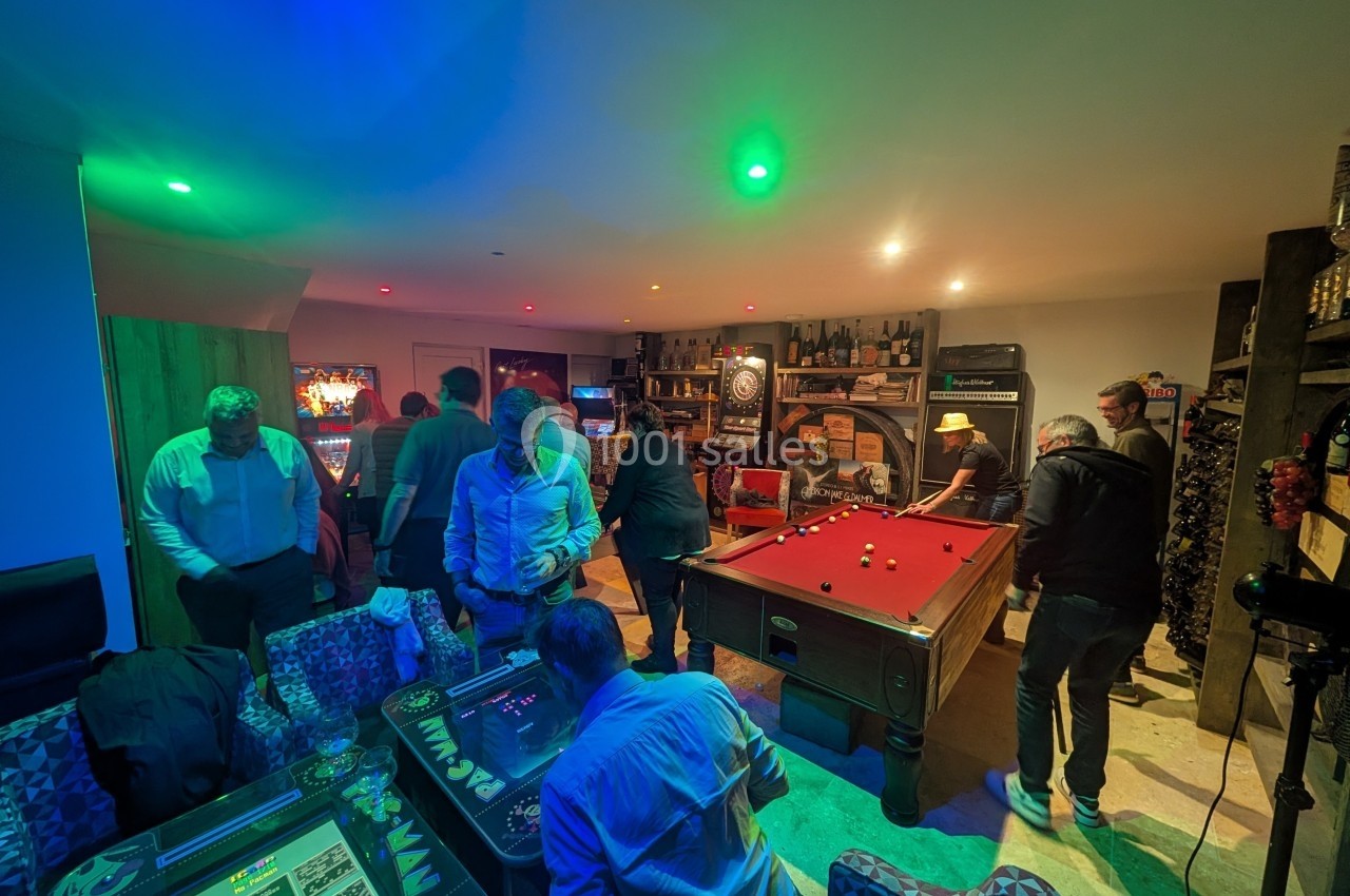Personnes jouant au billard et à des jeux d'arcade dans une salle éclairée par des lumières colorées.