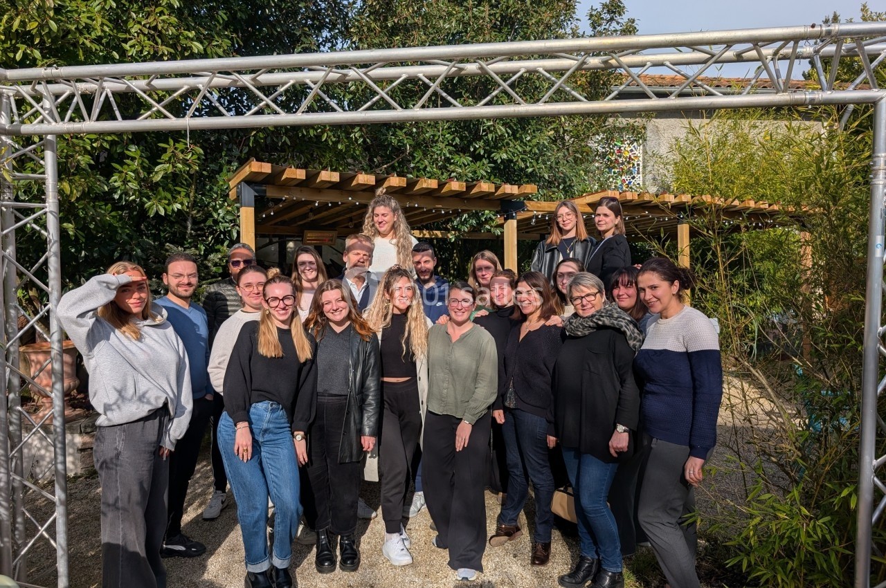 Groupe de personnes posant ensemble dans un jardin, entouré de végétation et de structures en bois et métal.