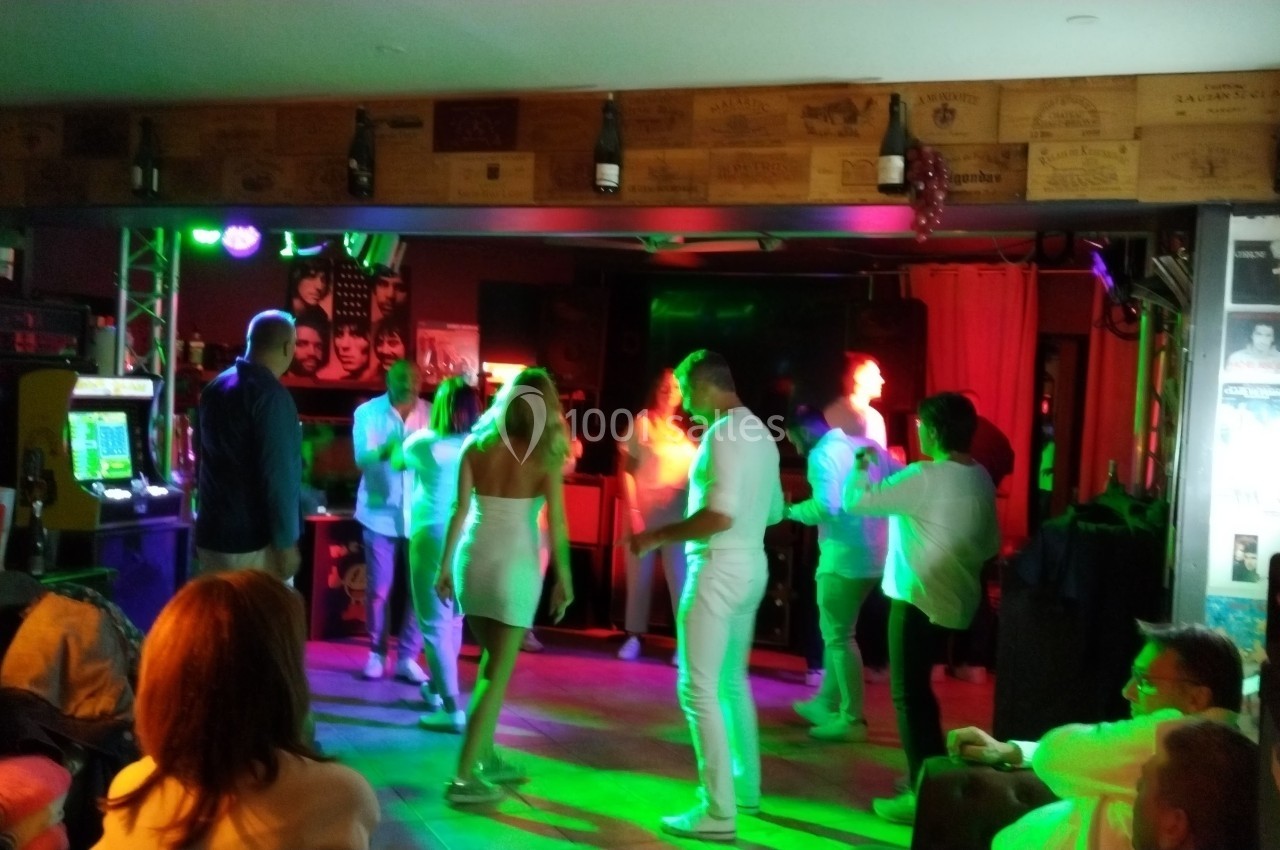 Personnes dansant dans un espace intérieur coloré par des lumières vives, entourées de spectateurs assis.