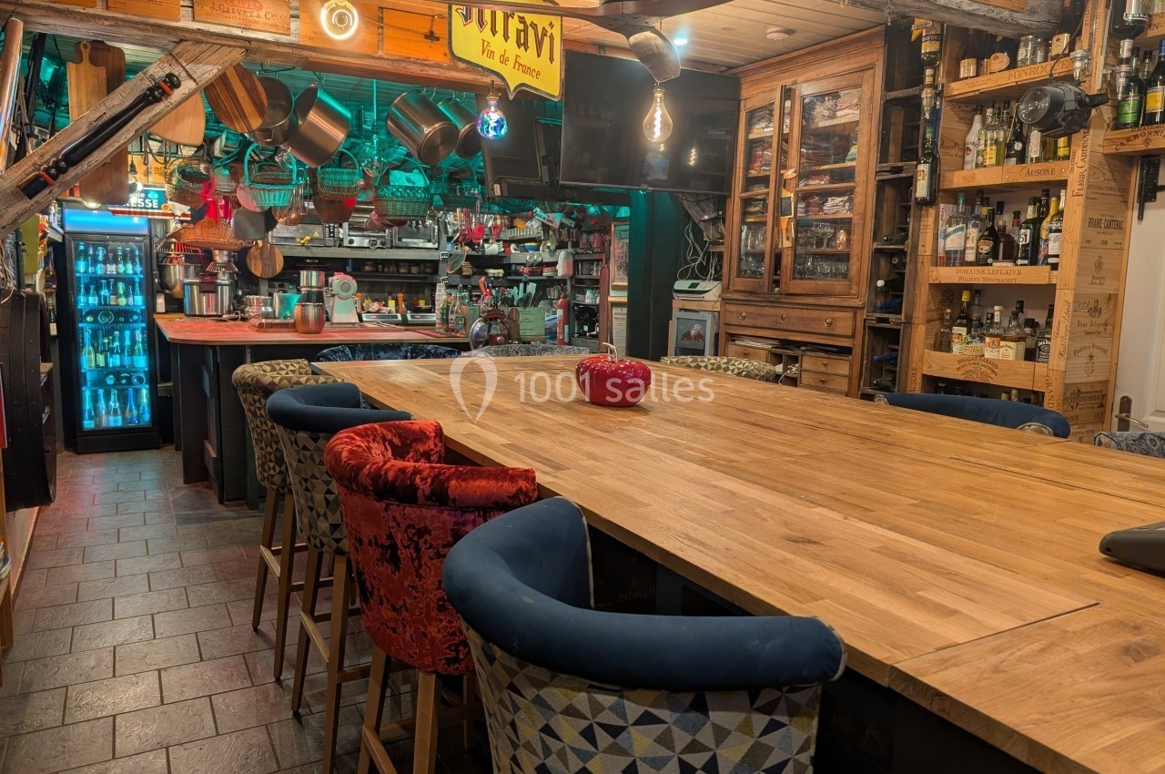 Cuisine ouverte avec grande table en bois entourée de chaises, étagères remplies et ambiance chaleureuse.