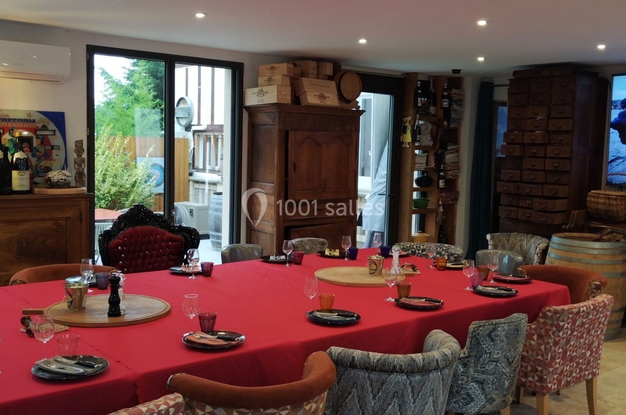 Salle à manger conviviale avec une grande table dressée, entourée de chaises variées, et un écran allumé en arrière-plan.