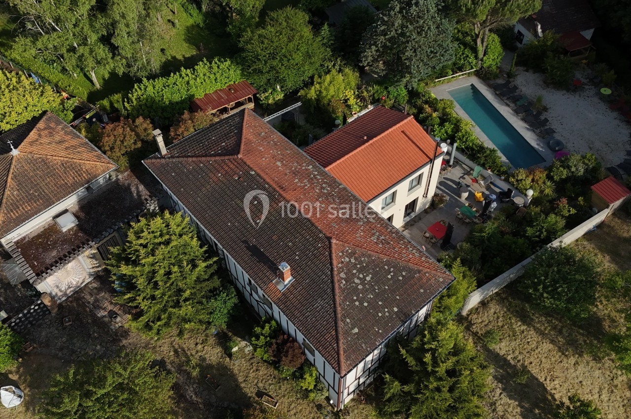 Vue aérienne d'une maison avec toit en tuiles, jardin arboré et piscine rectangulaire à proximité.