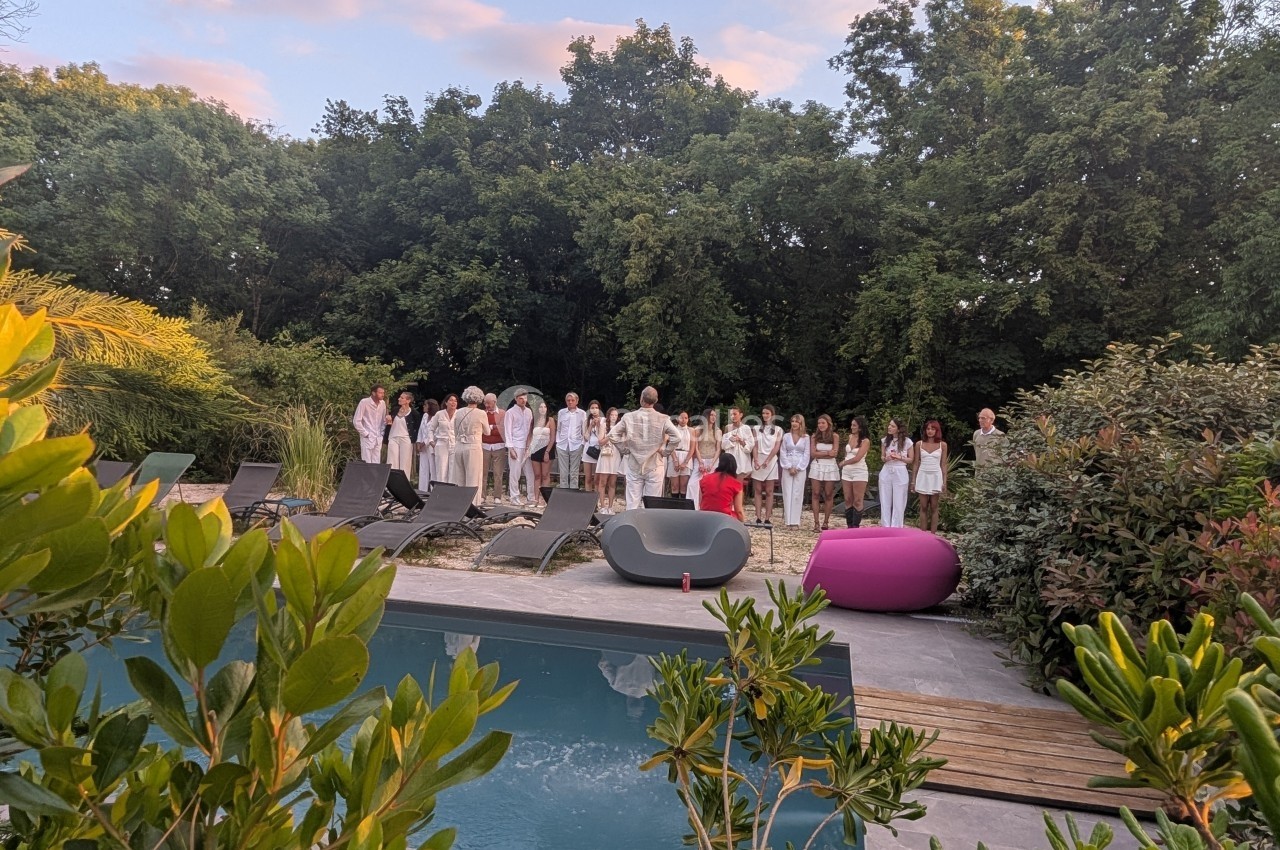 Groupe de personnes rassemblées près d'une piscine dans un jardin entouré de végétation.