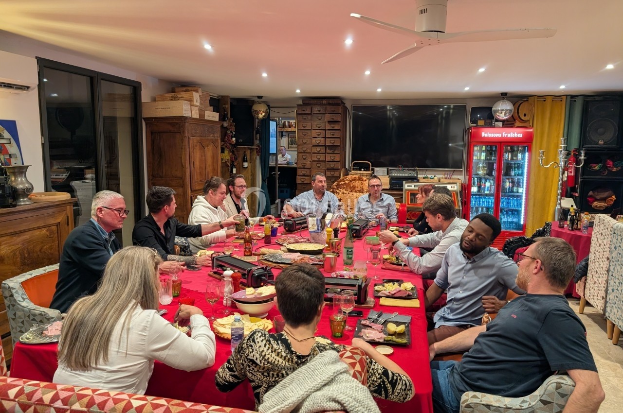 Groupe de personnes partageant un repas autour d'une grande table dans une salle chaleureuse et éclairée.