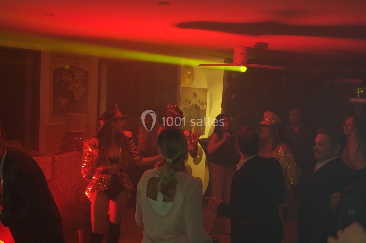 Personnes dansant et discutant dans une ambiance tamisée avec éclairage rouge lors d'une fête en intérieur.