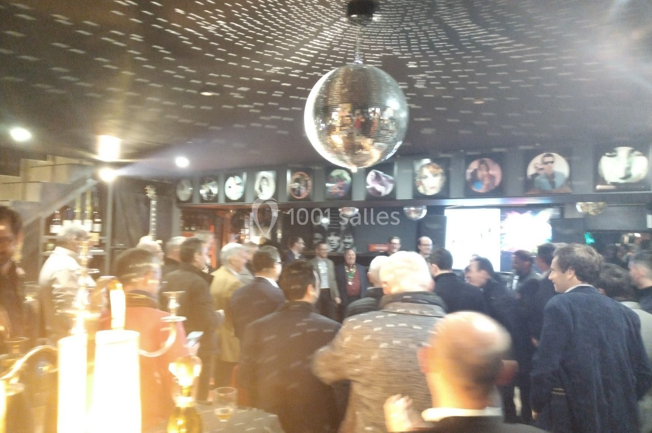 Groupe de personnes rassemblées dans un bar ou une salle festive avec une boule à facettes au plafond.