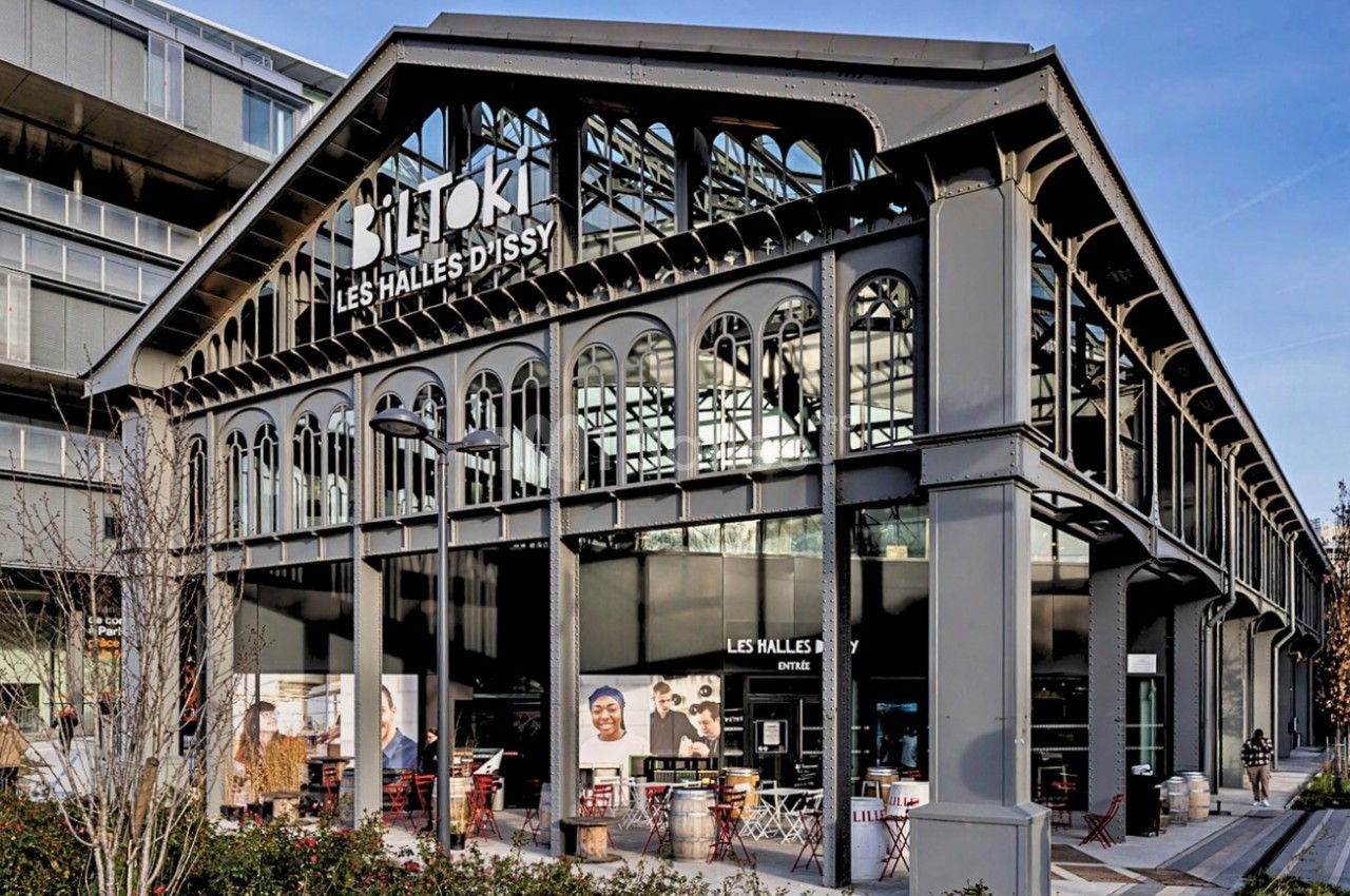 Façade d'un bâtiment industriel rénové abritant des commerces et restaurants, entouré d'espaces urbains modernes.