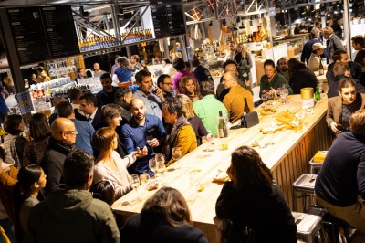 Terrasse extérieure avec tables et bancs en bois, entourée d'une clôture, vue sur des bâtiments modernes et un ciel dégagé.