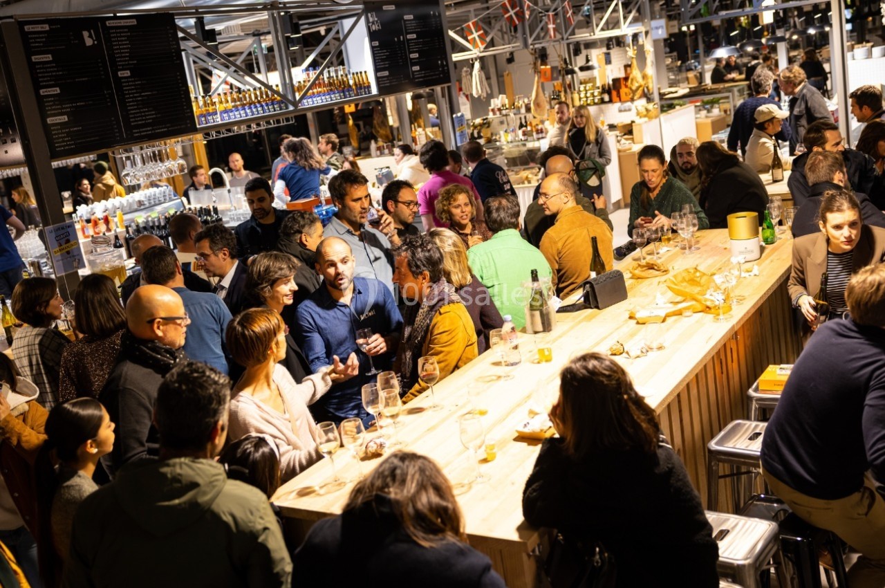 Groupe de personnes rassemblées autour d'un comptoir dans un espace animé, partageant boissons et conversations.