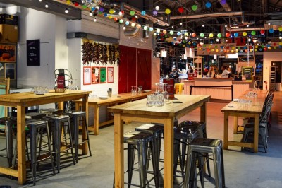 Terrasse extérieure avec tables et bancs en bois, entourée d'une clôture, vue sur des bâtiments modernes et un ciel dégagé.