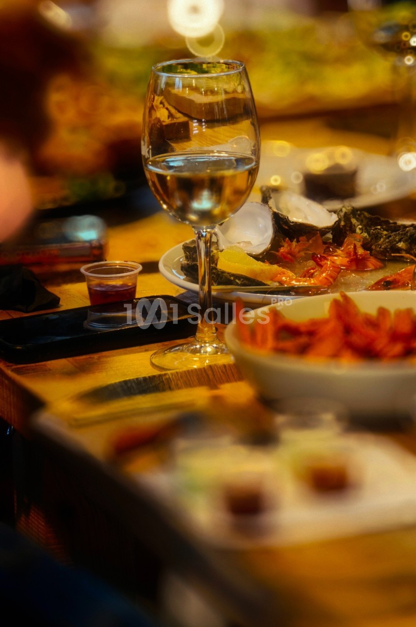 Verre d'eau sur une table en bois entourée de plats variés et d'autres verres lors d'un repas convivial.